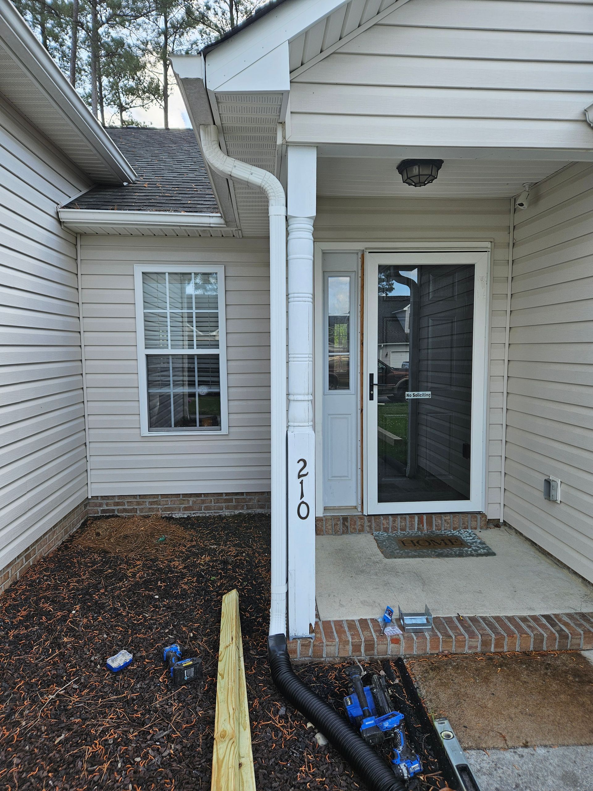 Exterior of a house with a front door, window, and porch. Tan siding, white trim, and a dark roof.
