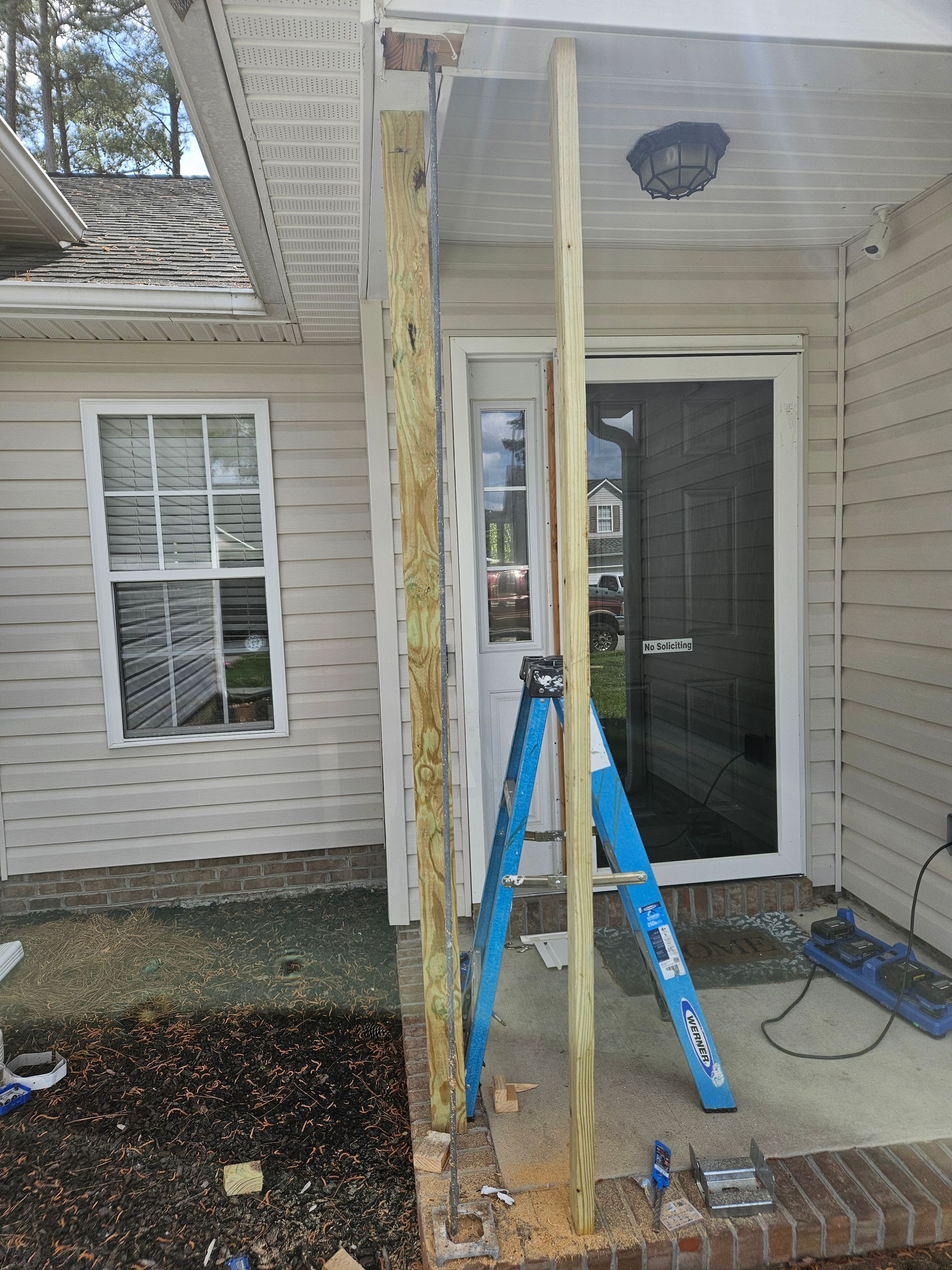 Exterior view of a house porch with a ladder and two wooden posts being installed.