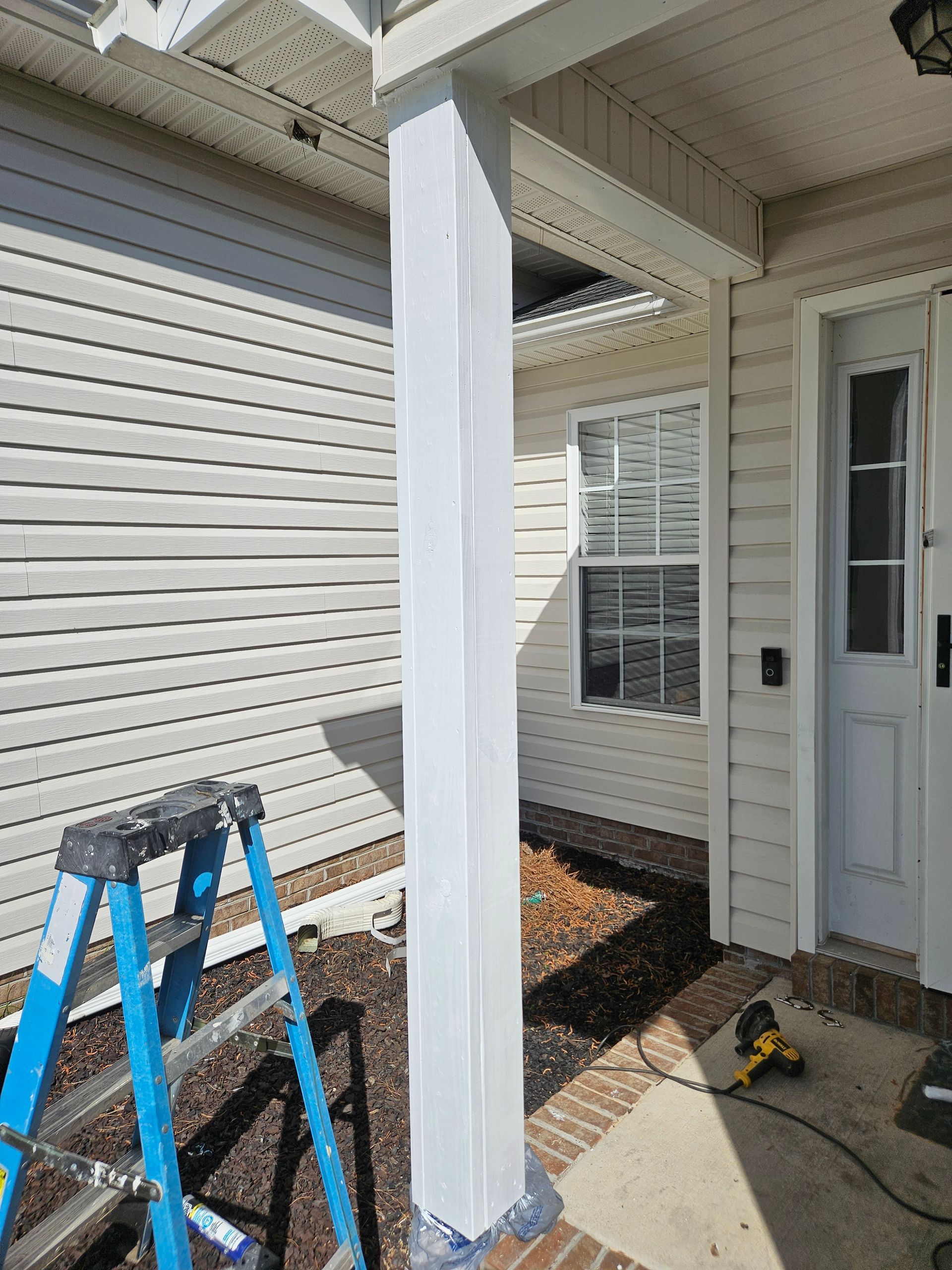 White column on a porch next to a house with siding; blue ladder is in the frame.