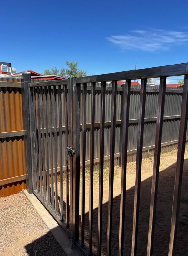 A metal fence with a wooden fence behind it