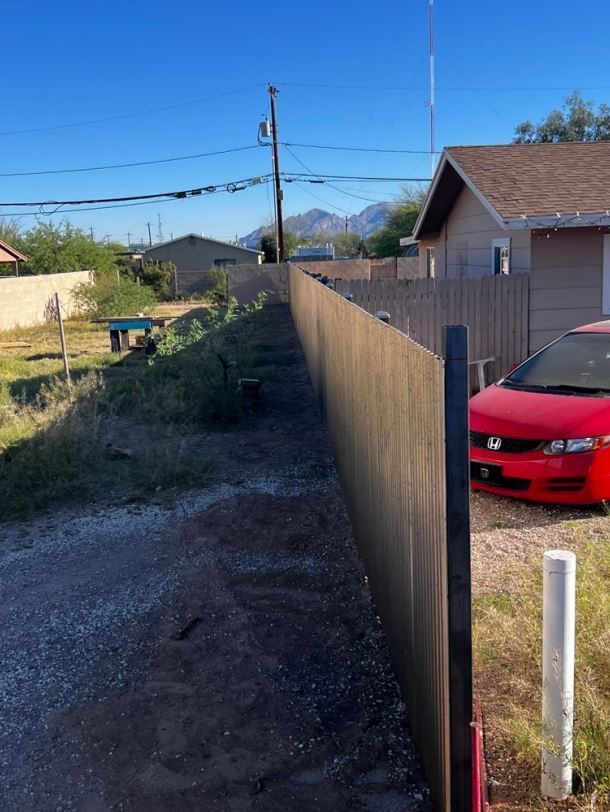A red car is parked next to a wooden fence