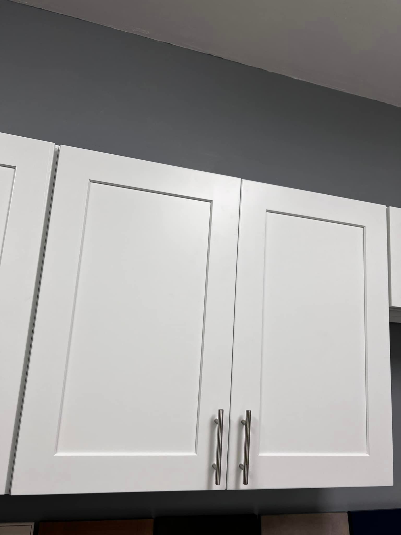 A kitchen with white cabinets and a gray wall