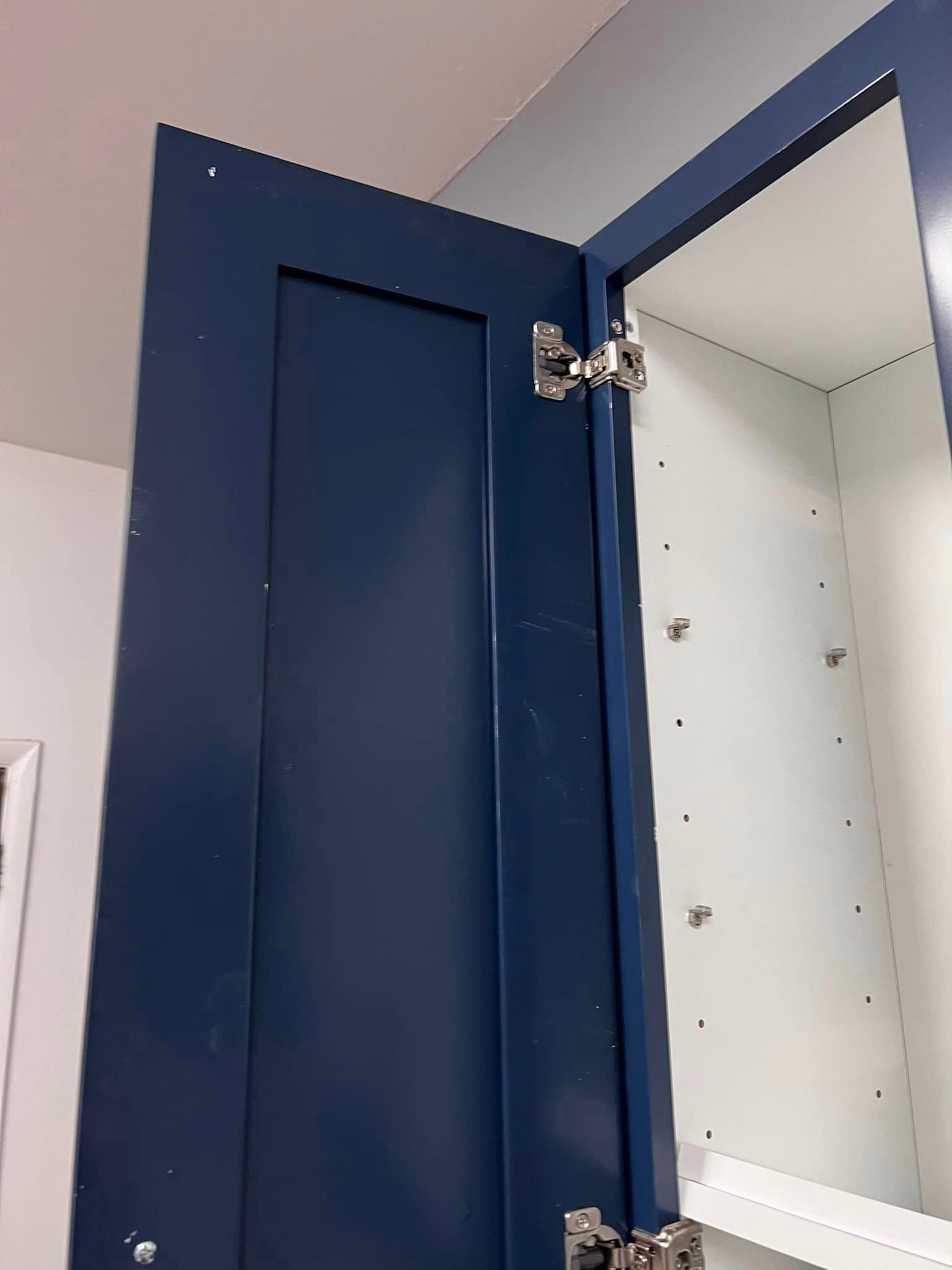 A blue cabinet with the door open in a bathroom.