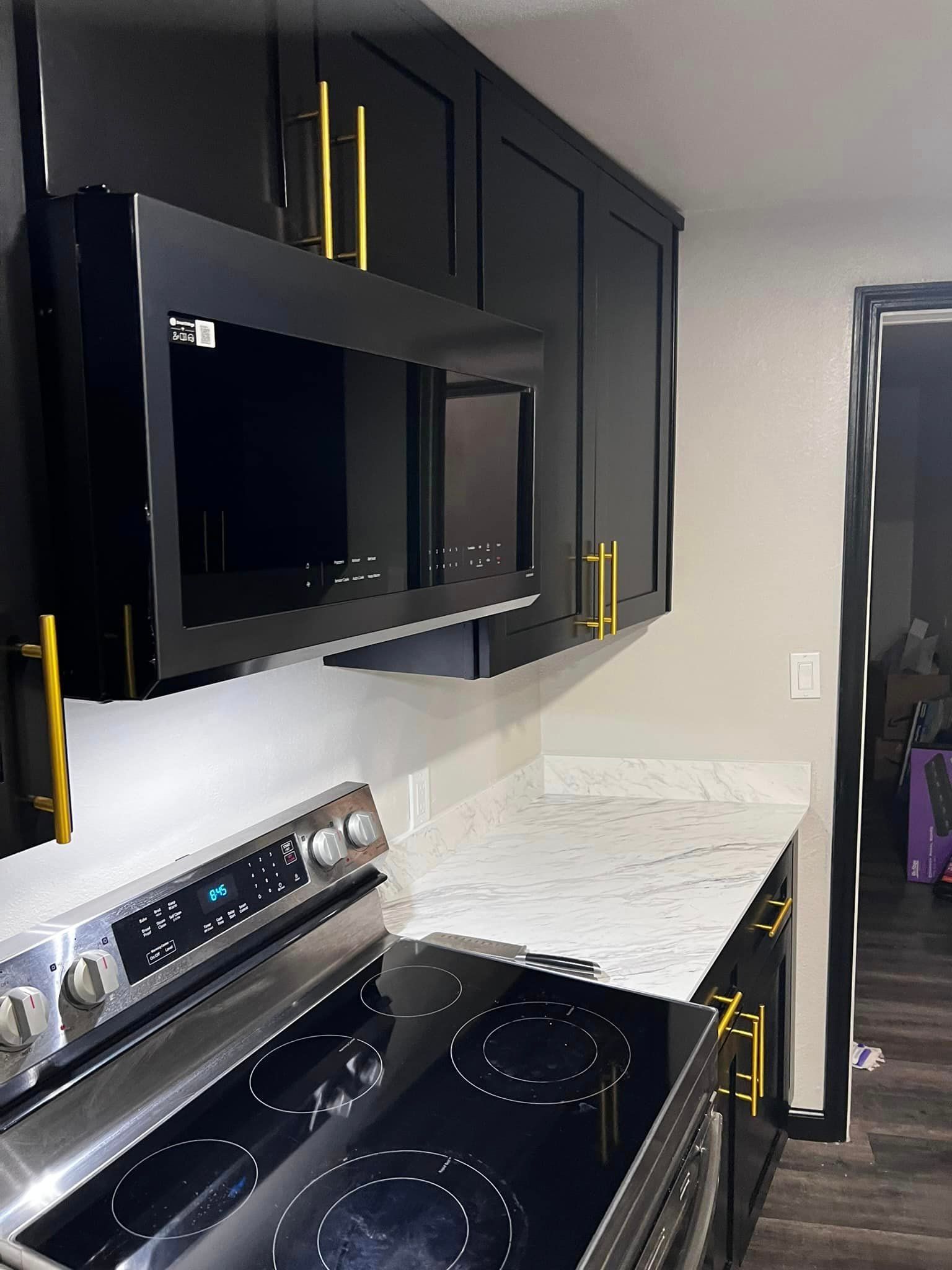 A kitchen with black cabinets , a stove , a microwave , and a marble counter top.
