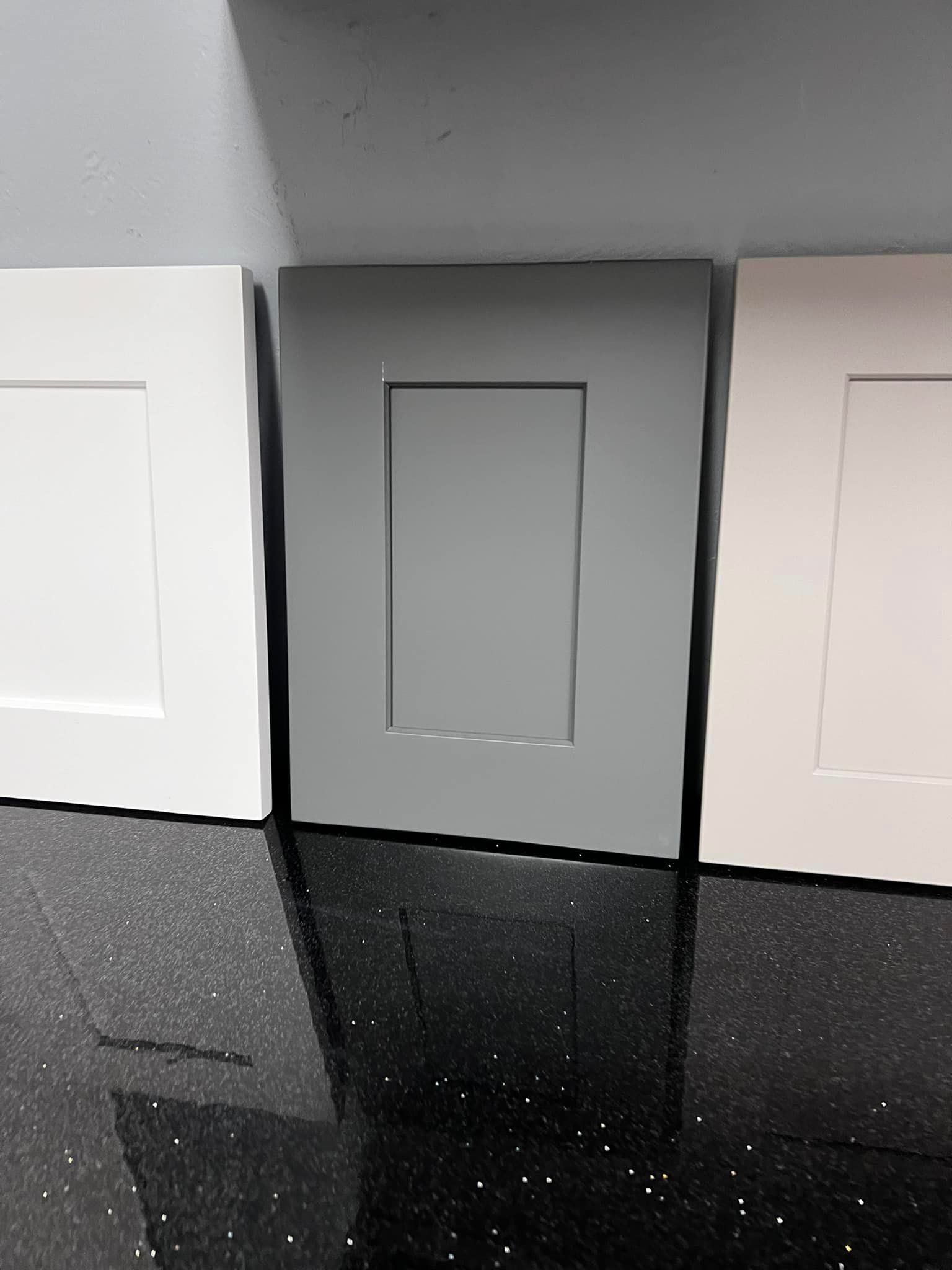 Three different colored cabinet doors are sitting on a black counter top