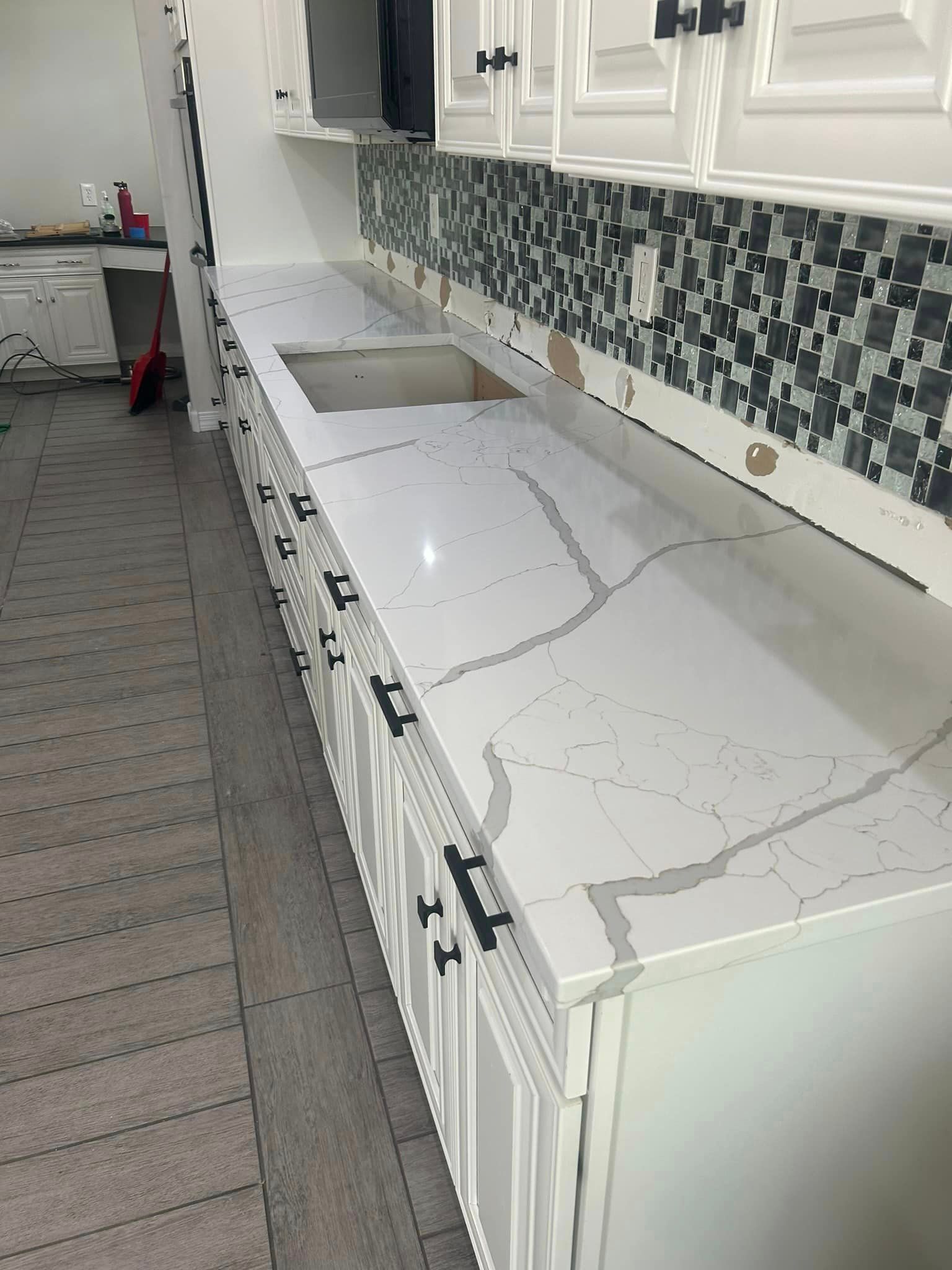 A kitchen with white cabinets , a sink , and a quartz counter top.