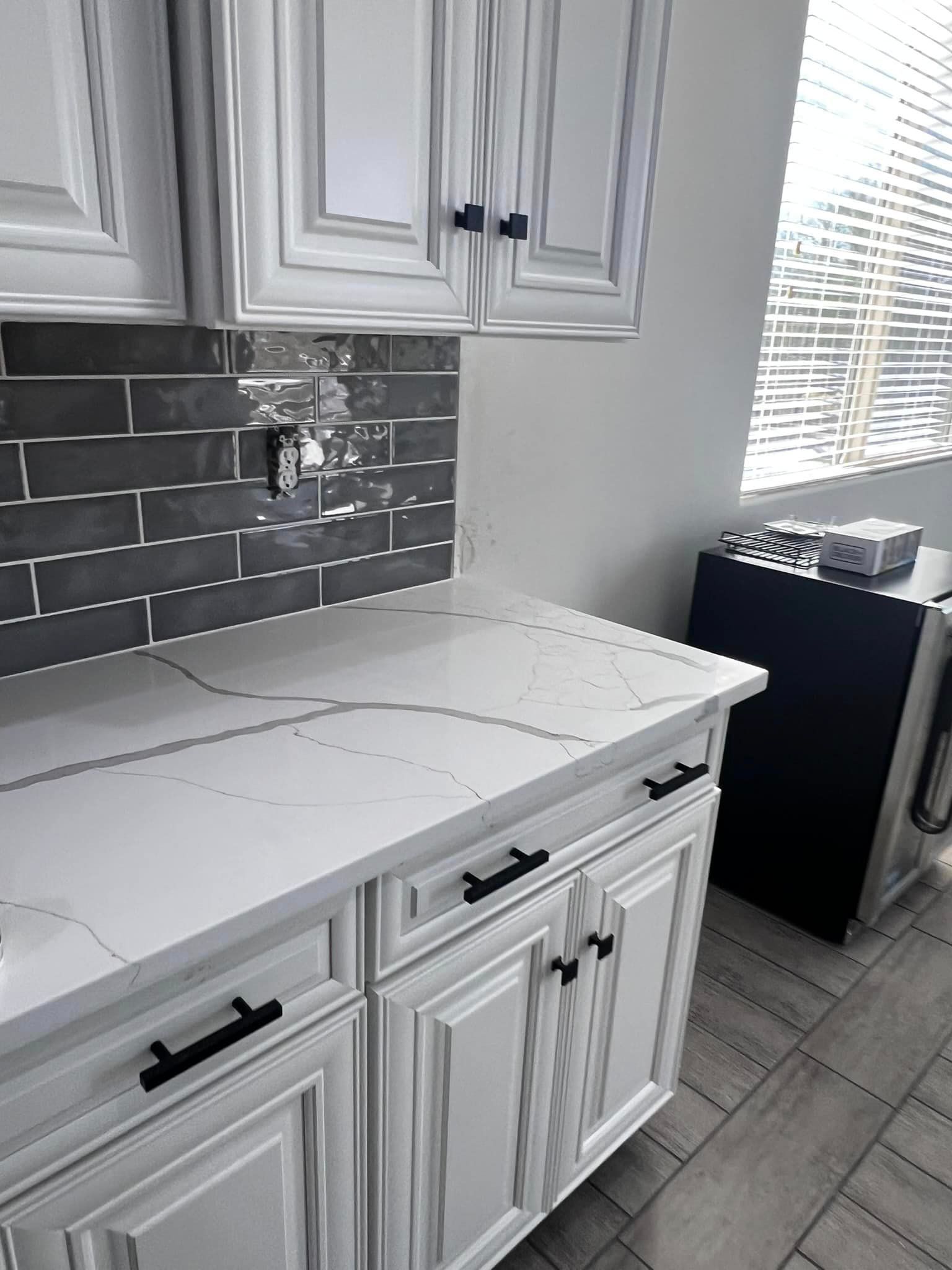 A kitchen with white cabinets and black handles and a white counter top.