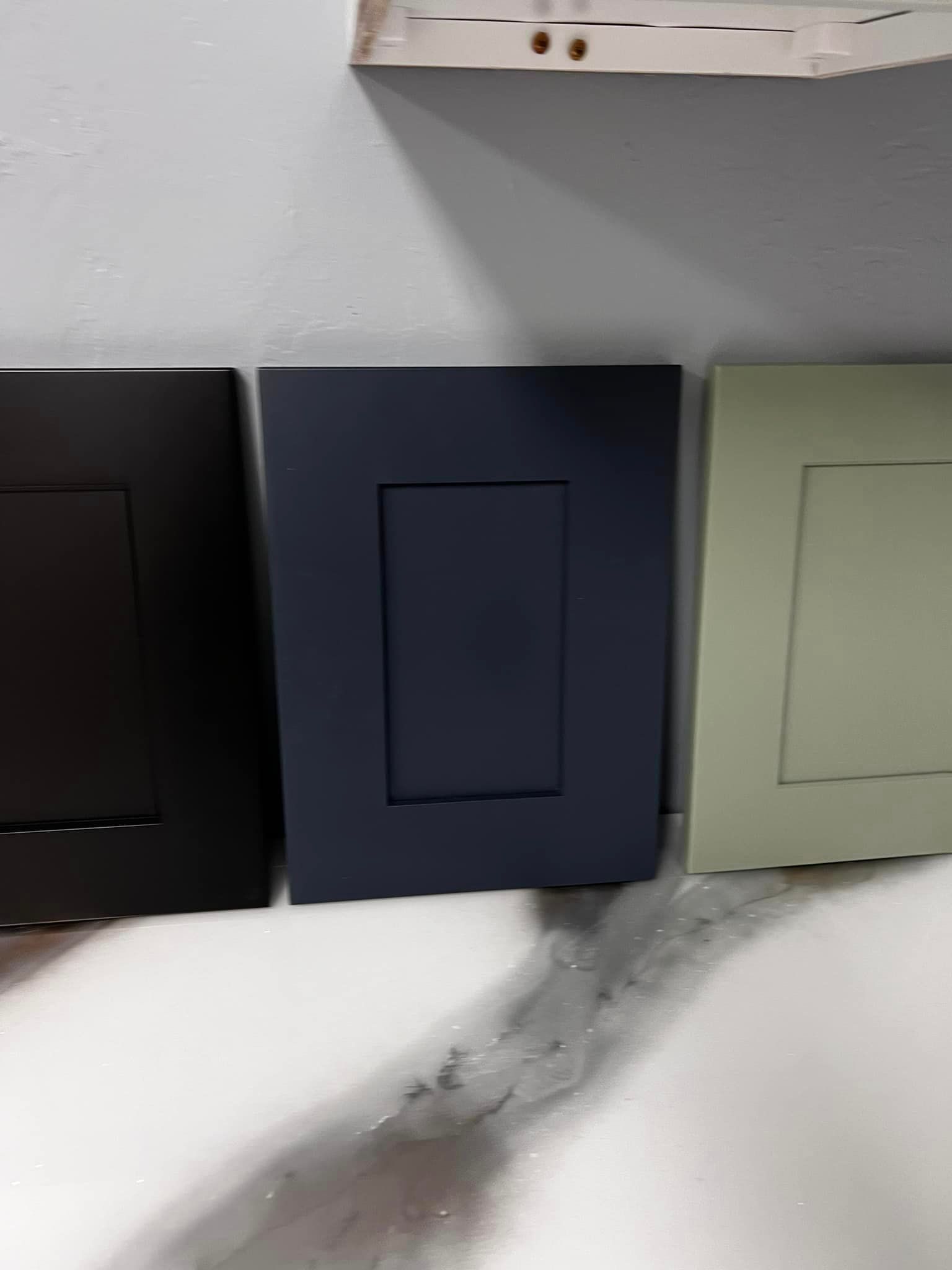 Three different colored cabinet doors are sitting next to each other on a shelf.