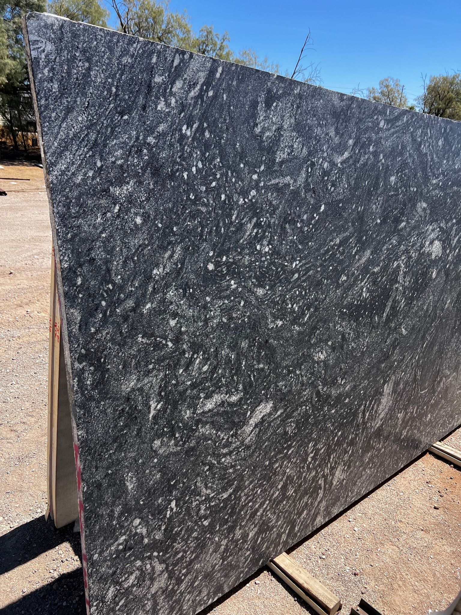 A large black granite slab is sitting on top of a dirt field.