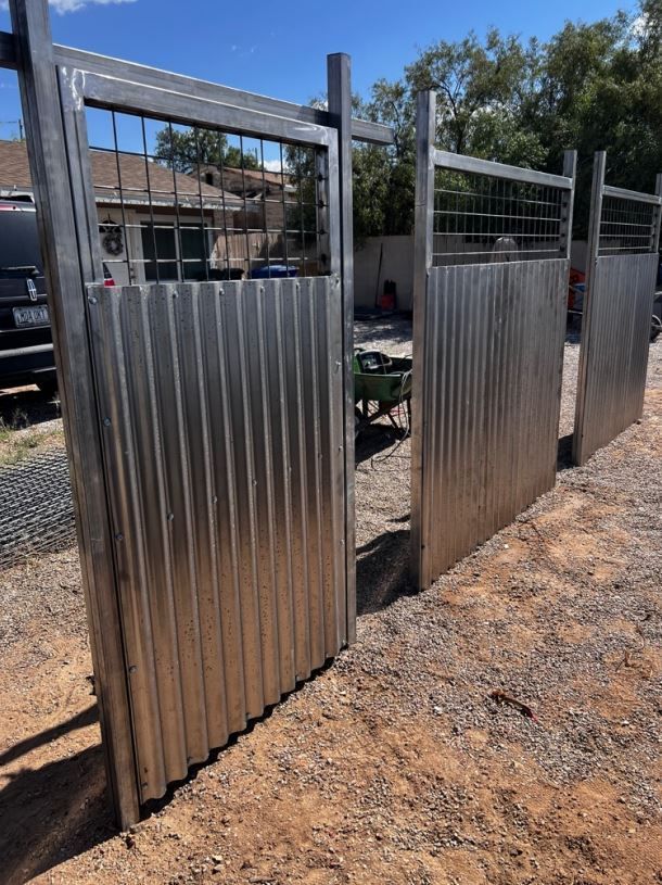 A fence made of corrugated metal is sitting on top of a dirt field.