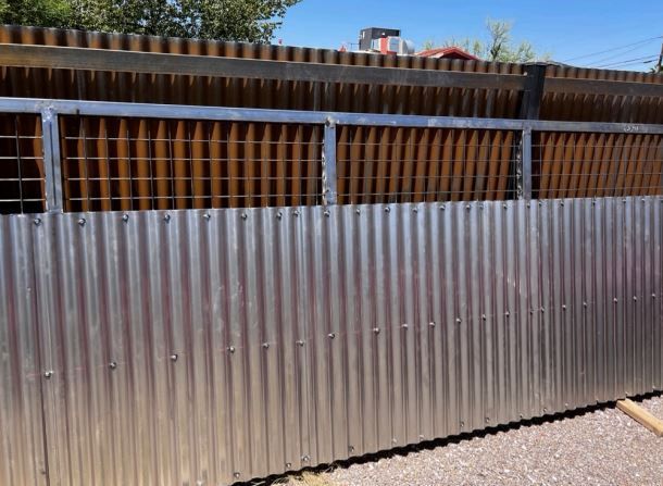 A metal fence with a wooden fence behind it