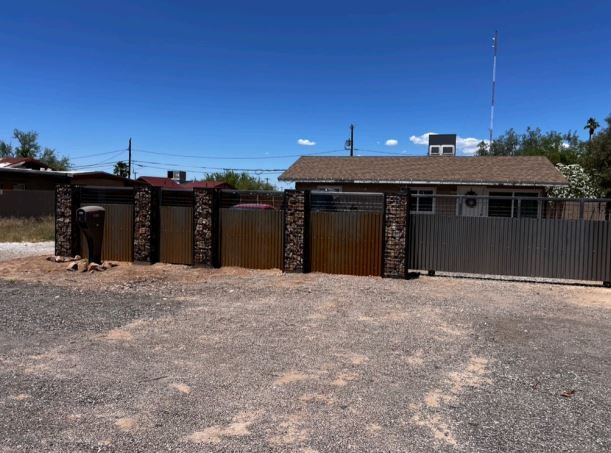 A house with a fence around it and a lot of gravel in front of it.