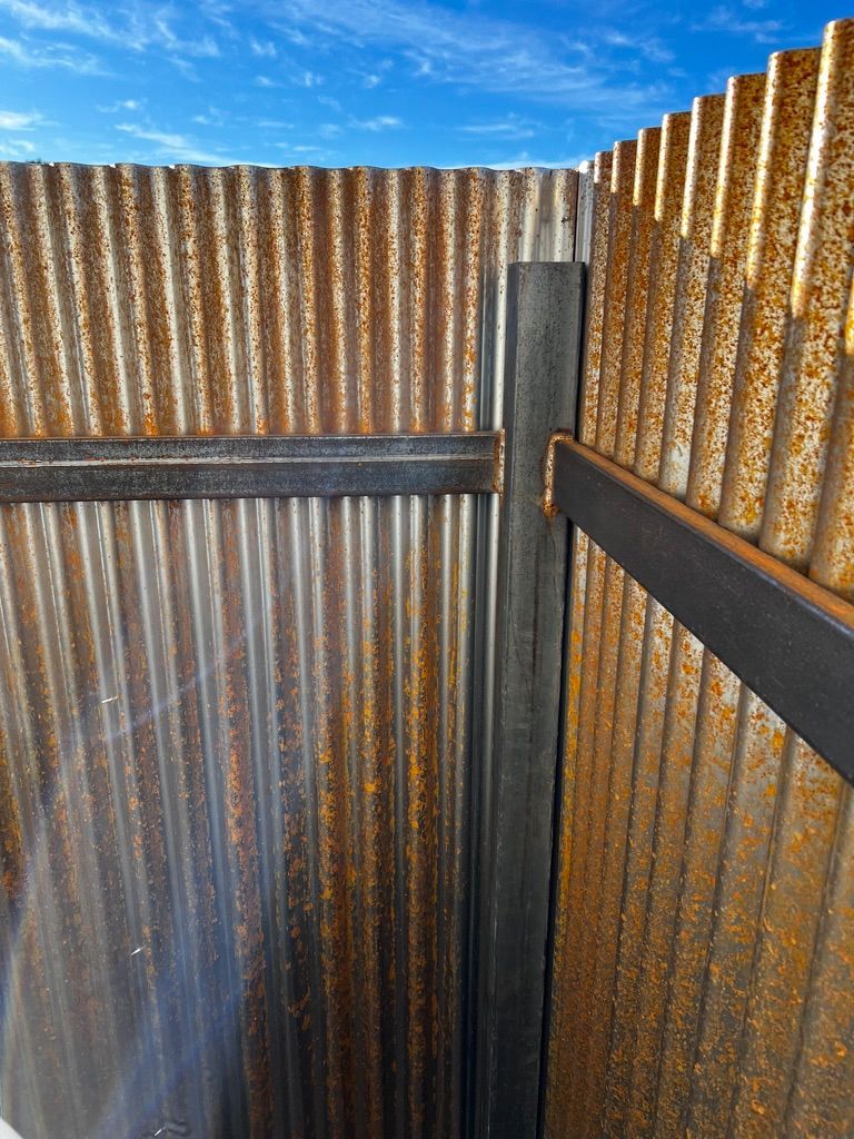 A rusty metal fence with a blue sky in the background