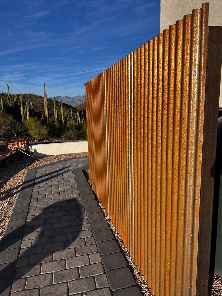 A rusty metal fence is sitting next to a brick walkway.