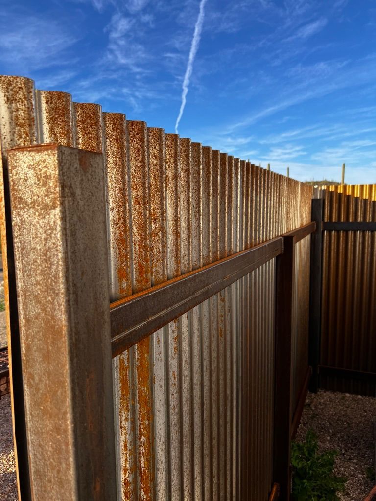 A rusty metal fence with a blue sky in the background