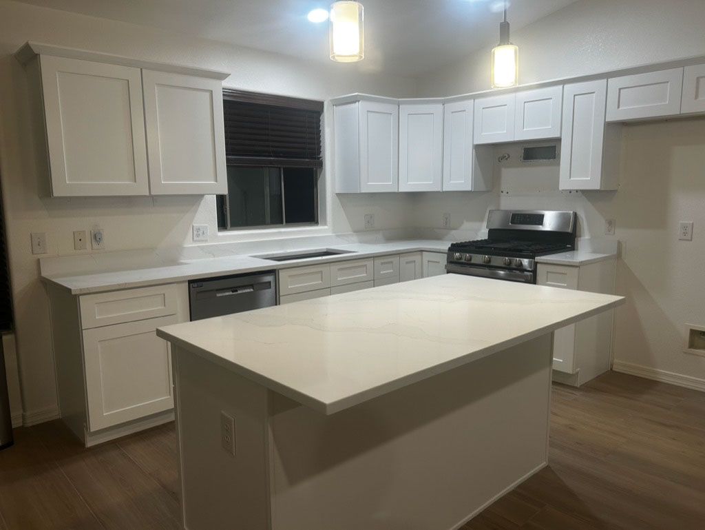 White kitchen with cabinets, countertops, and an island. Stainless steel appliances and wood flooring.