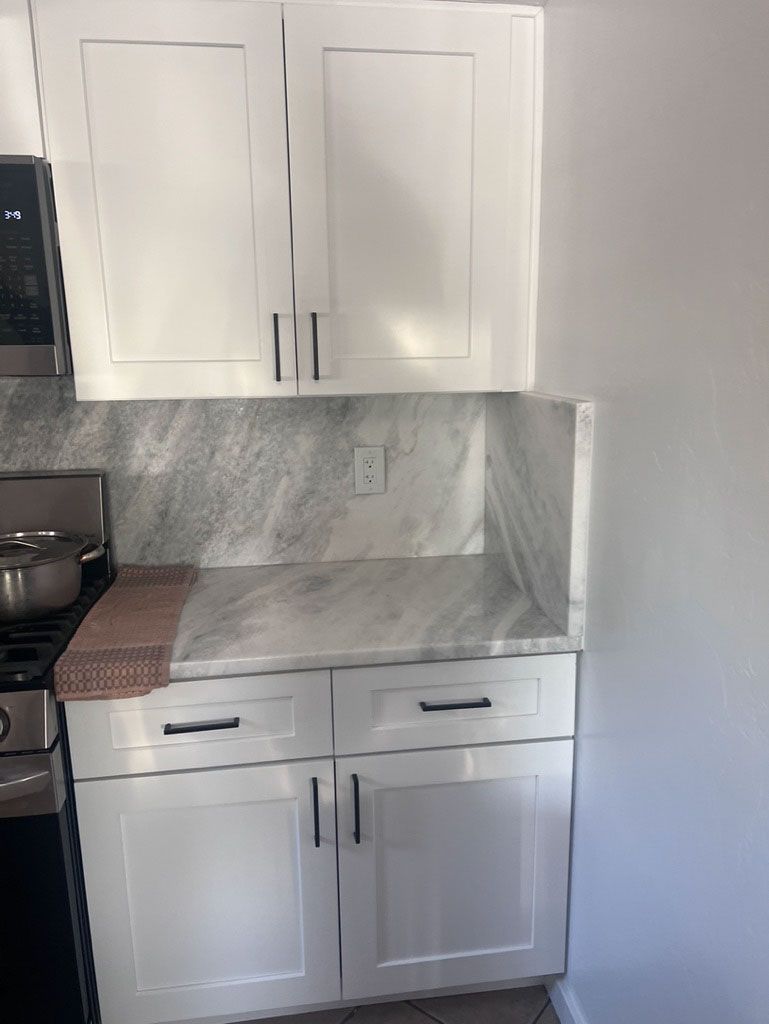 White kitchen cabinets and countertop with a marbled backsplash. A stove is visible on the left.