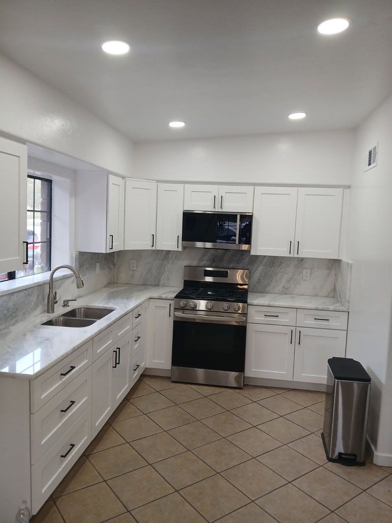 White kitchen with stainless steel appliances and light-colored countertops and backsplash. 