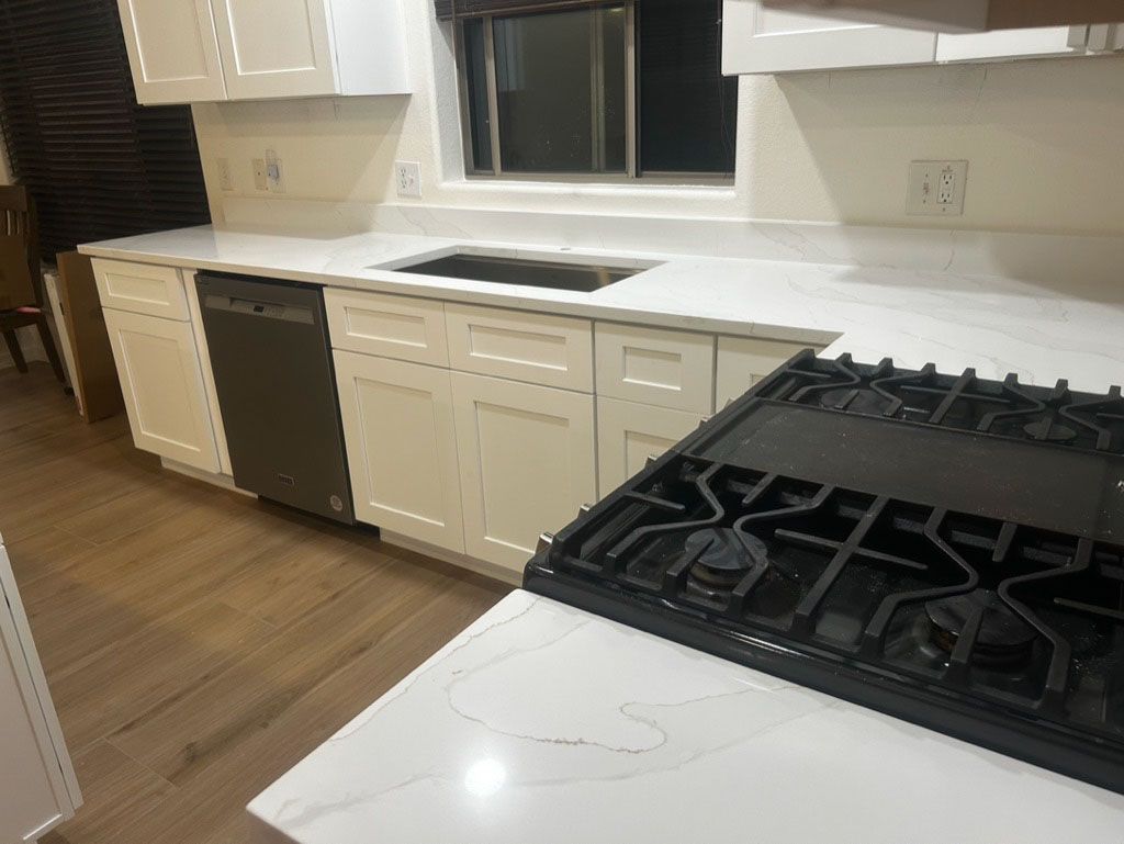 A kitchen with white cabinets, countertops, and a black stovetop. A black dishwasher is visible. The room has wooden floors.