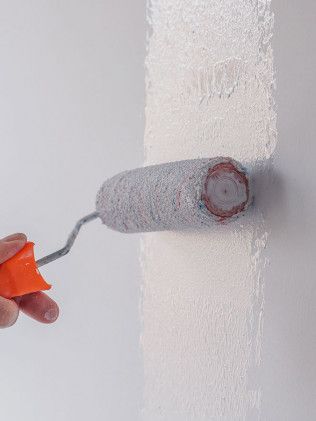 A person is painting a wall with a paint roller.