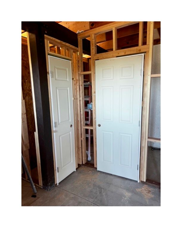 Two white doors are sitting next to each other in a room under construction.