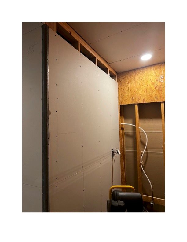 A large piece of drywall is being installed on a wall in a room.