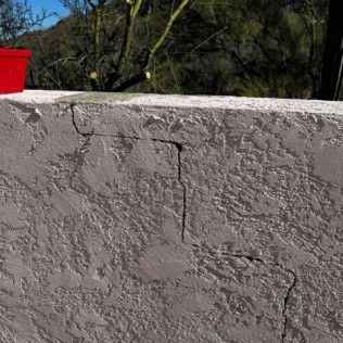 A cracked concrete wall with a red cup on top of it.