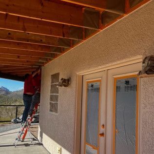 A man is standing on a ladder on the side of a house.