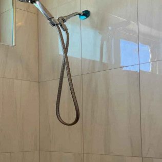 A shower head with a hose attached to it is hanging from a tiled wall.