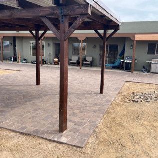 A wooden pergola is sitting on top of a brick patio in front of a house.