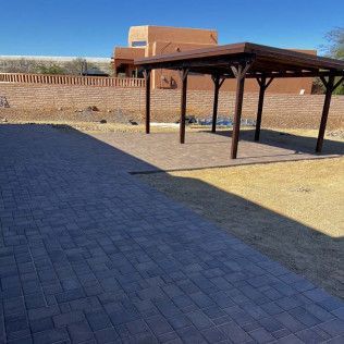 A brick driveway with a wooden pergola in the middle of it.