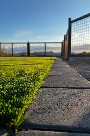 A concrete walkway leading to a grassy field with a fence in the background.