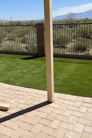 A patio with a fence and a lush green lawn.