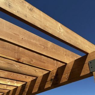 A close up of a wooden pergola with a blue sky in the background.