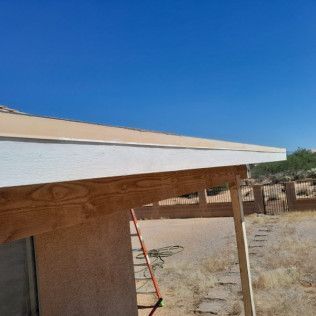 A wooden structure with a white trim on the roof is being built in the desert.