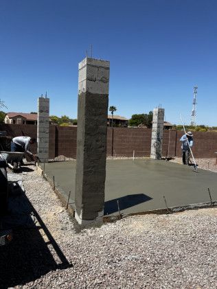 A concrete floor is being poured in a yard with pillars in the background.