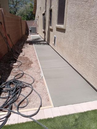 A concrete walkway is being built in the backyard of a house.