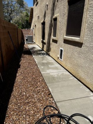 A concrete walkway leading to a house next to a wooden fence.
