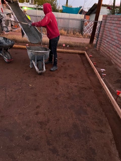 A man in a red hoodie is pouring concrete into a wheelbarrow.