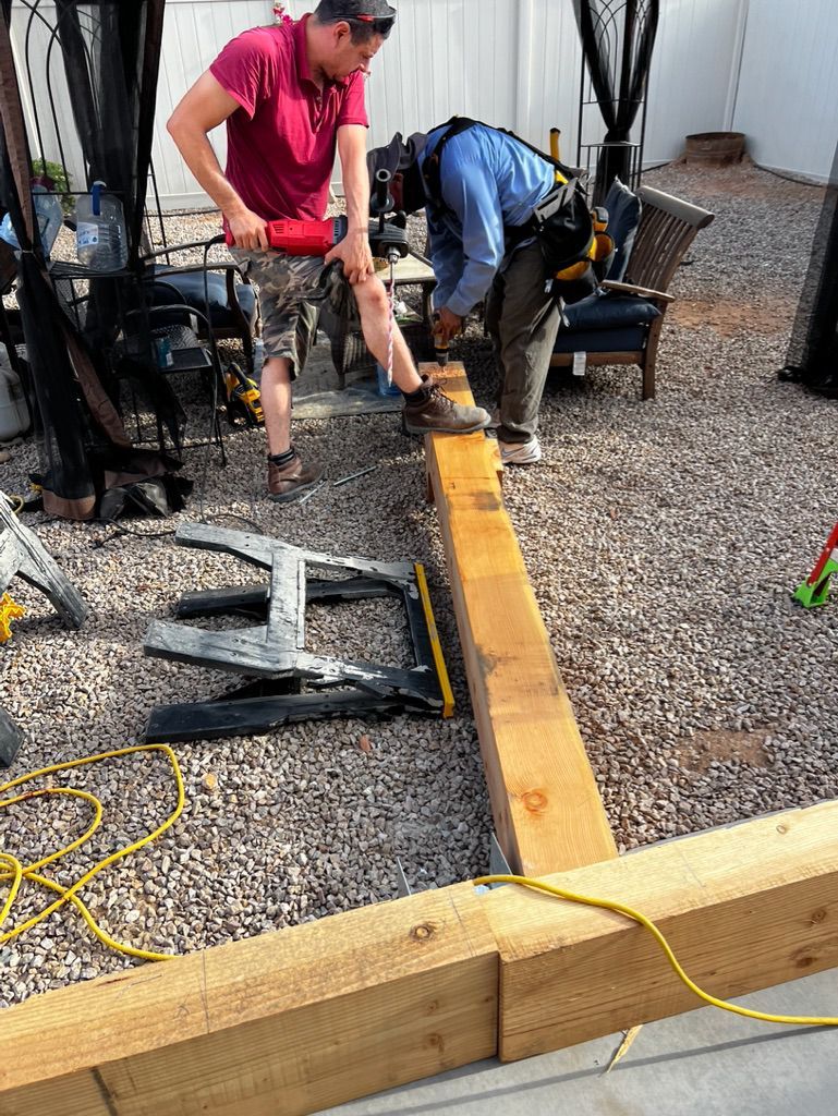 Two men are working on a wooden beam in a gravel yard.