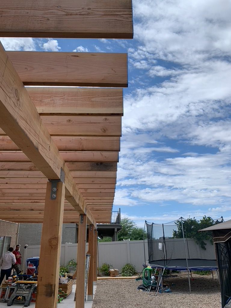 A wooden pergola is being built in a backyard.