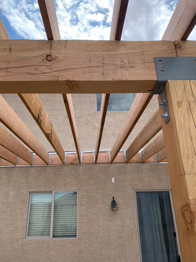 A wooden pergola is being built on the side of a house.