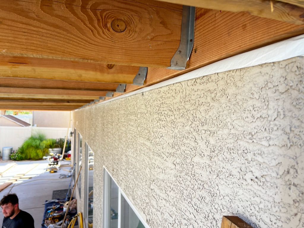 A man is working on the side of a house under a wooden roof.