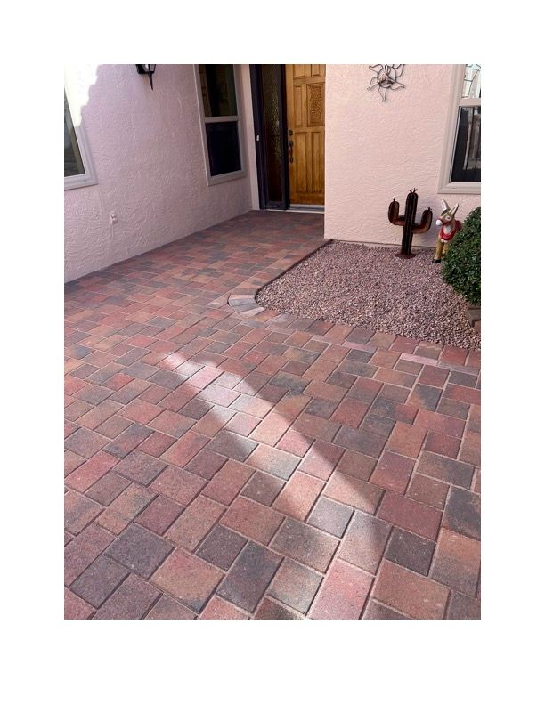 A brick walkway in front of a house with a cactus in the background.