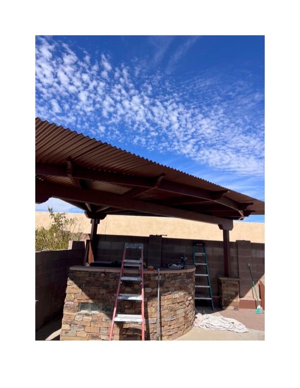 A ladder is sitting under a wooden roof next to a stone wall.
