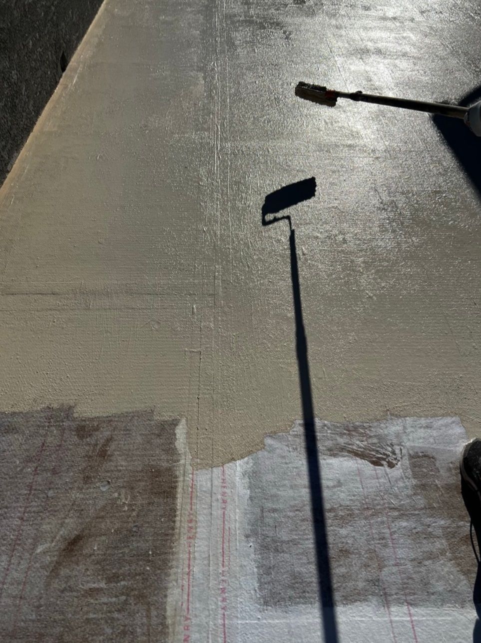 A person is painting a sidewalk with a roller.