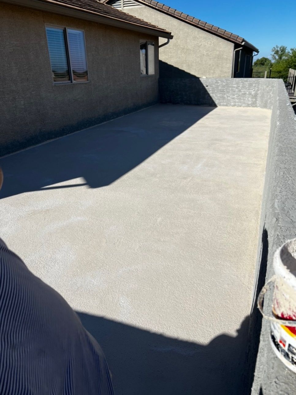 A person is standing in front of a house with a bucket of paint in the foreground.