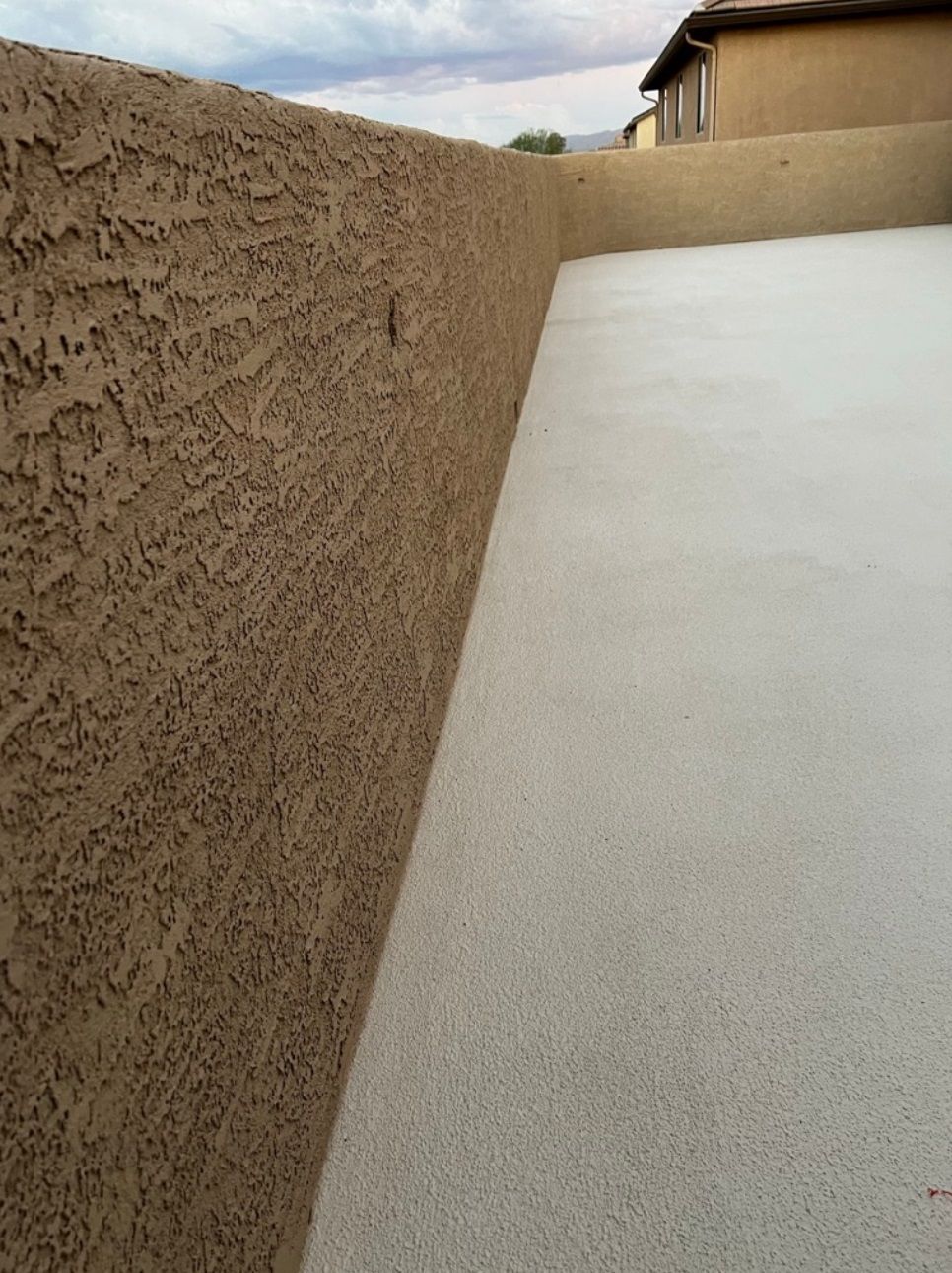 A brown wall with a white concrete walkway in front of it