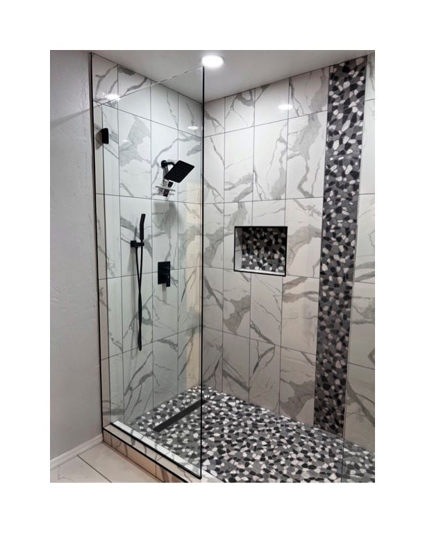 A walk in shower with marble tiles and a mosaic floor.