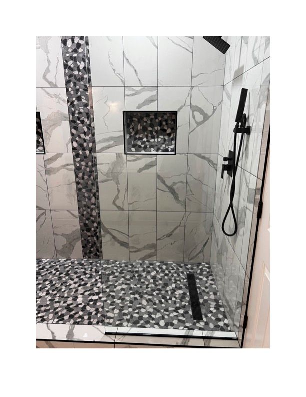 A walk in shower with marble tiles and a black shower head.
